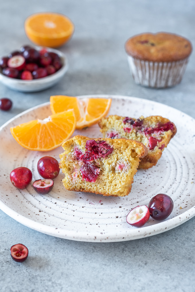Cranberry orange muffins cut in half on a plate with orange and cranberries