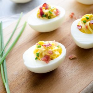 Deviled eggs with bacon on a cutting board with chives