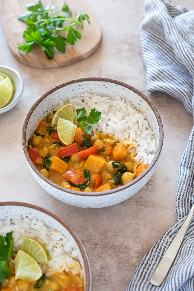 Chickpea curry in a bowl with rice, lime wedges and cilantro