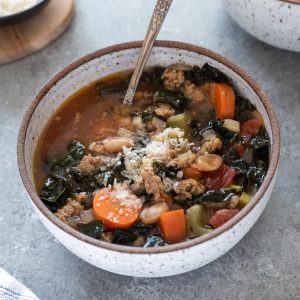 Italian sausage kale soup in a white bowl with spoon digging in