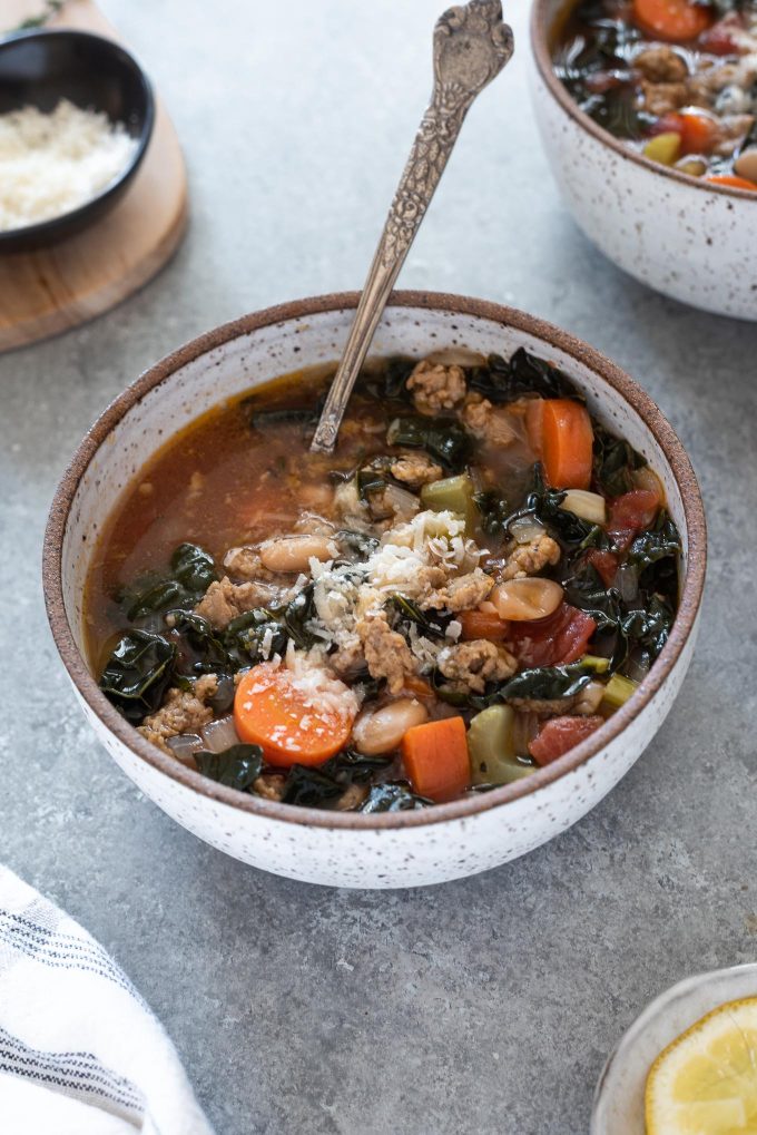 Italian sausage kale soup in a white bowl with spoon digging in
