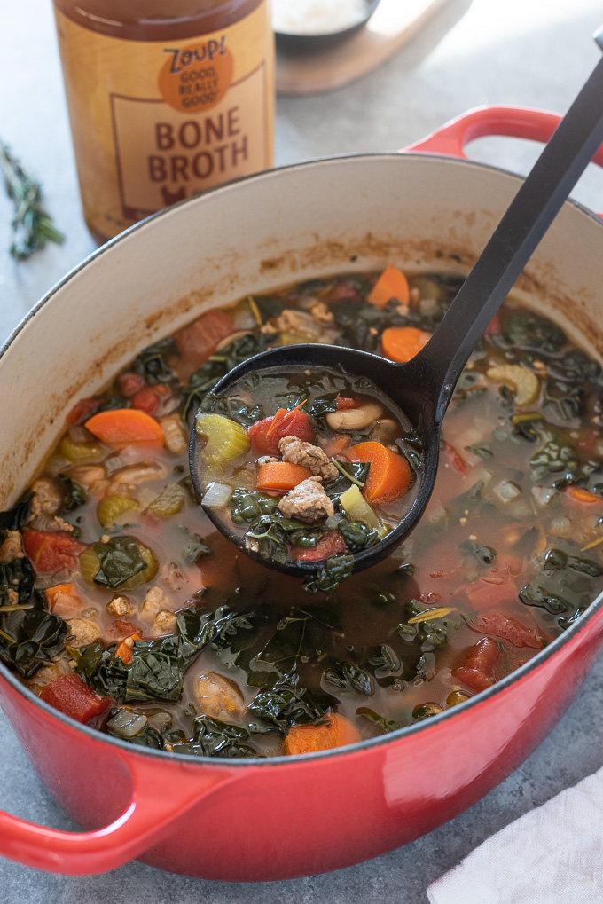 Ladle full of sausage and kale soup over a Dutch oven