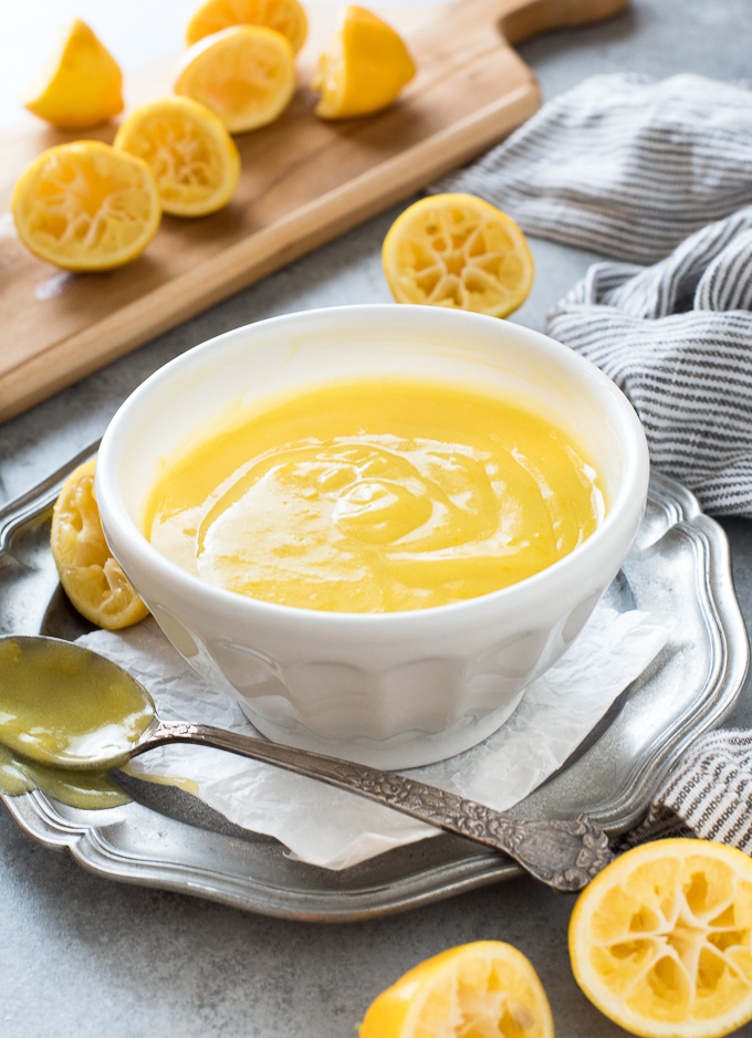 Homemade lemon curd in a bowl with juiced lemons all around