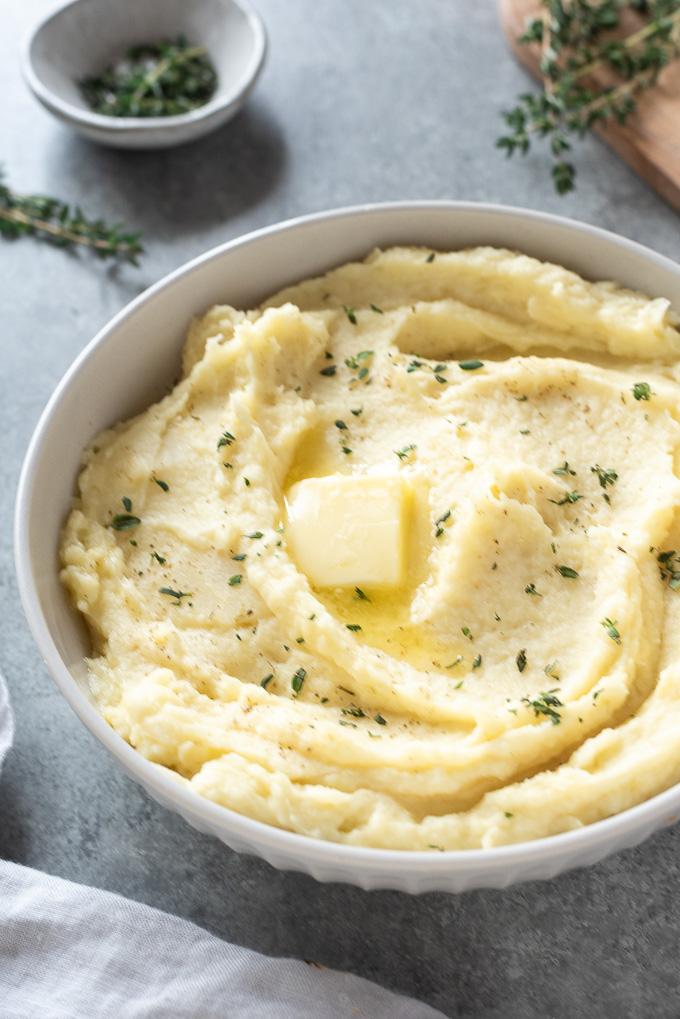 Parsnip puree in a white bowl with butter and thyme leaves on top