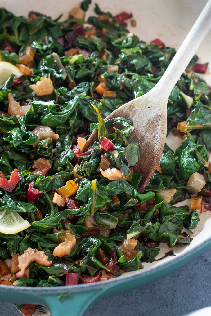Wooden spoon digging into a Dutch oven filled with sautéed Swiss chard
