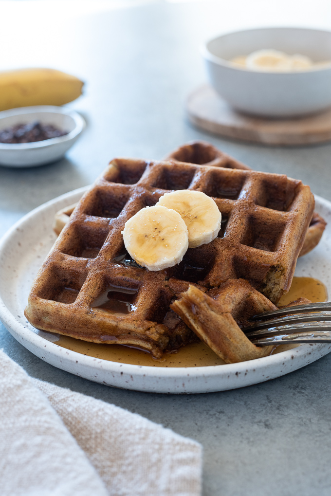 Banana waffles on a plate with sliced banana and maple syrup