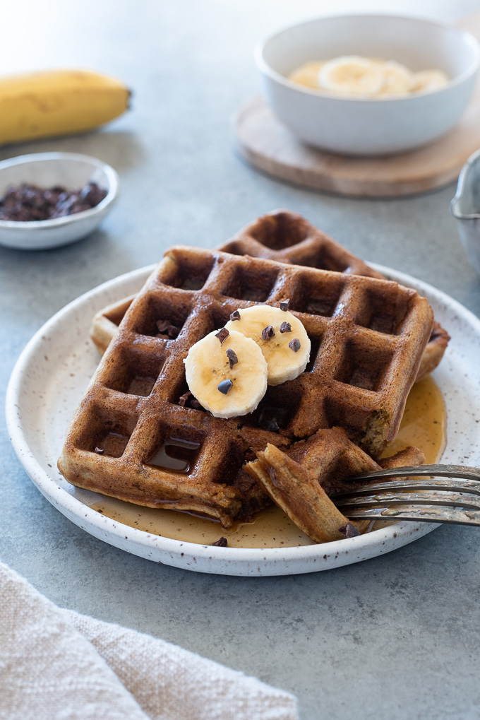 Banana oat waffles on a plate with banana and cacao nibs on top