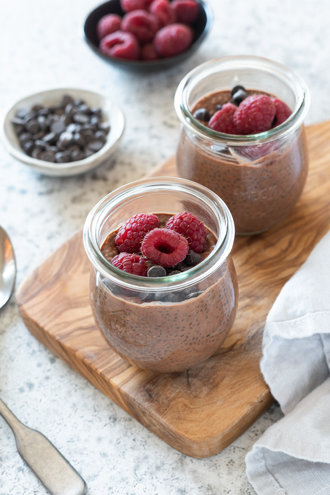 Chocolate chia pudding in jars topped with raspberries and chocolate chips