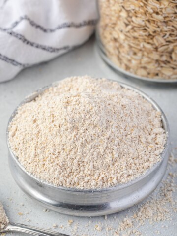 Oat flour in a bowl with jar of oats behind