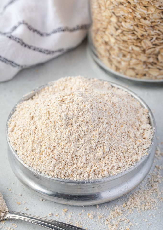 Oat flour in a bowl with jar of oats behind