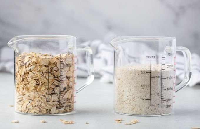 A measuring cup with 1 cup rolled oats next to one with 3/4 cup oat flour