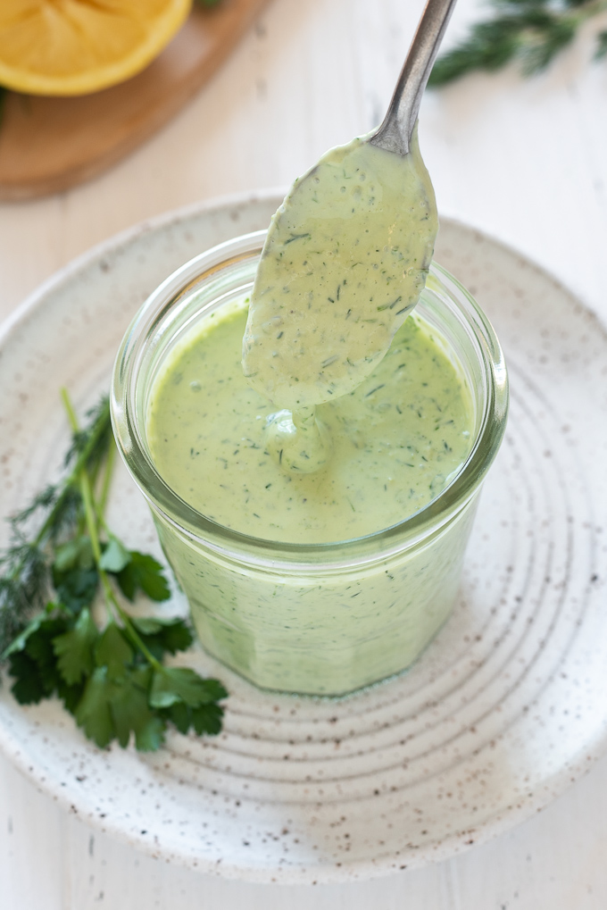Green goddess dressing drizzling from a spoon into a jar