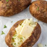 Air fryer baked potatoes with pats of butter and parsley