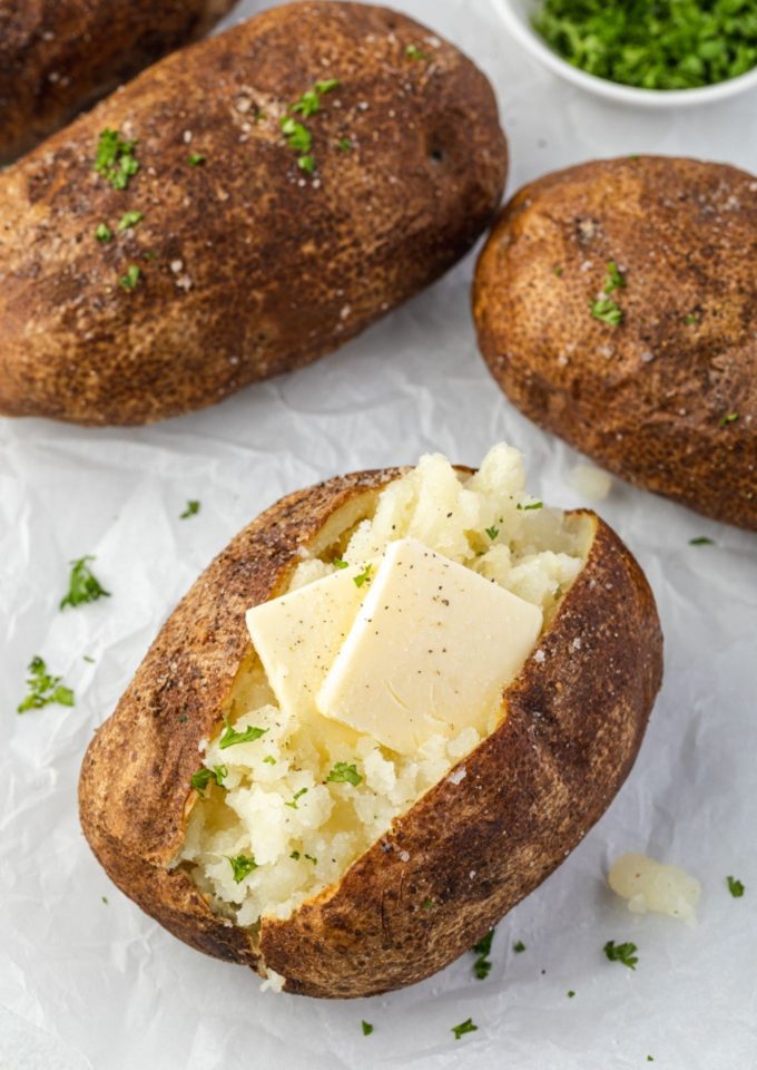 Air fryer baked potatoes with pats of butter and parsley
