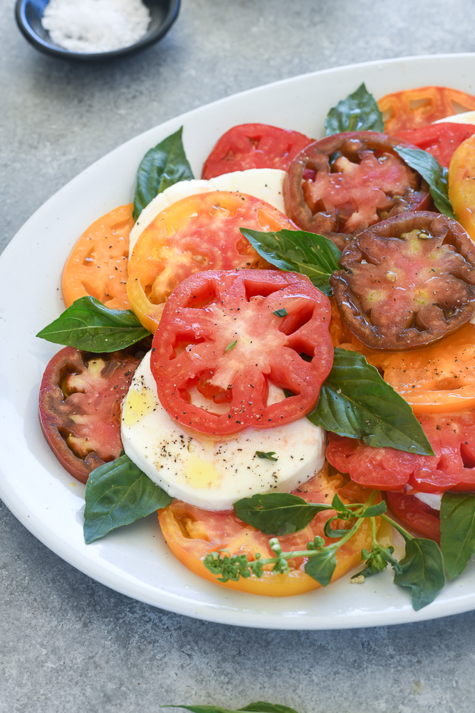 Tomato mozzarella salad layered on a white platter with basil