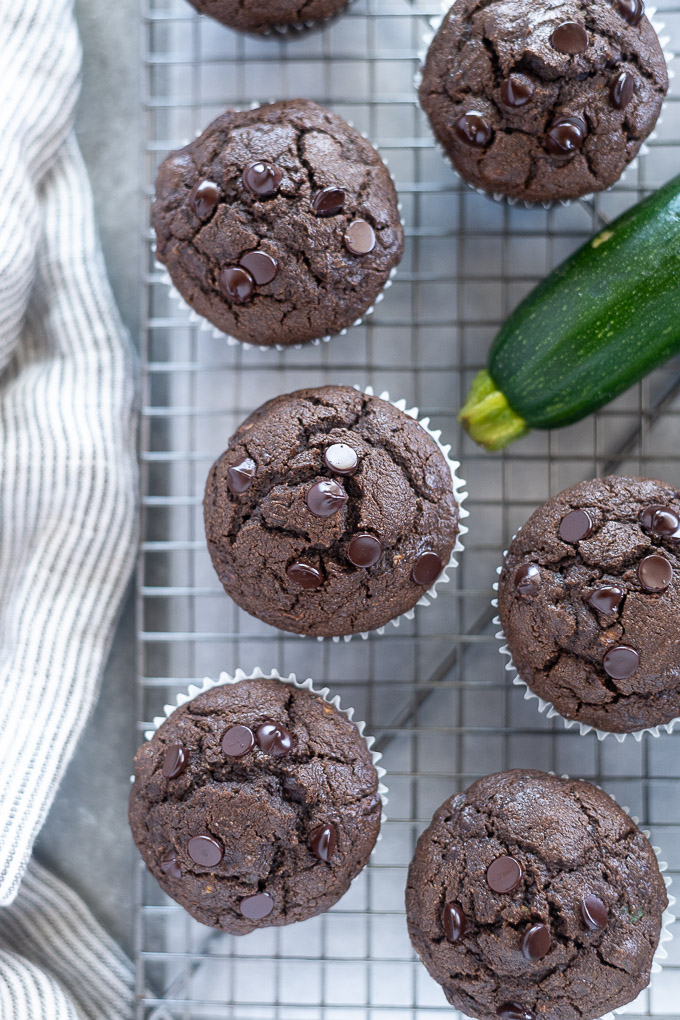 Double chocolate zucchini muffins on a wire rack with zucchini