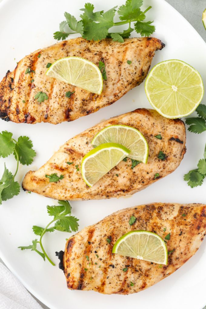 Grilled tequila lime chicken on a platter with lime slices and cilantro