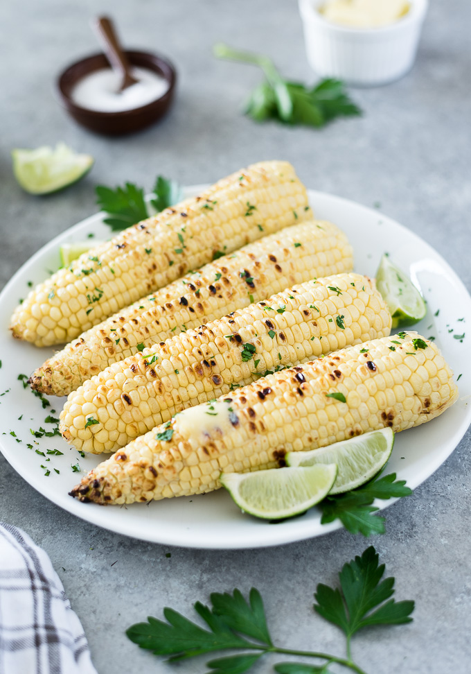 Ears of grilled corn on a white plate with lime