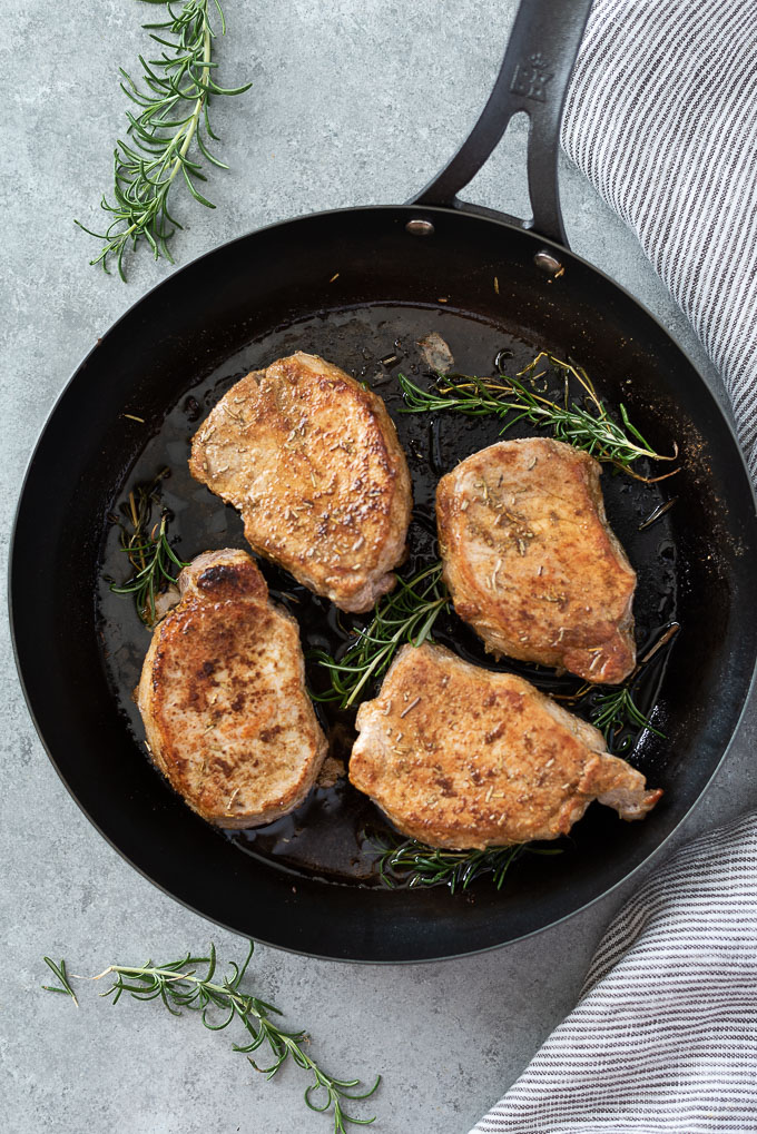 Baked pork chops in a skillet with rosemary sprigs