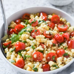 Spoon buried in a bowl of corn and tomato salad