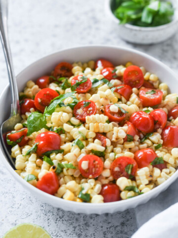 Spoon buried in a bowl of corn and tomato salad