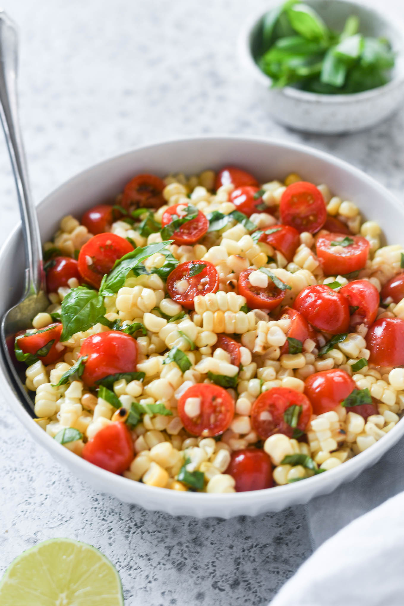 Close up of Fresh Corn and Tomato Salad in white serving bowl with serving spoon
