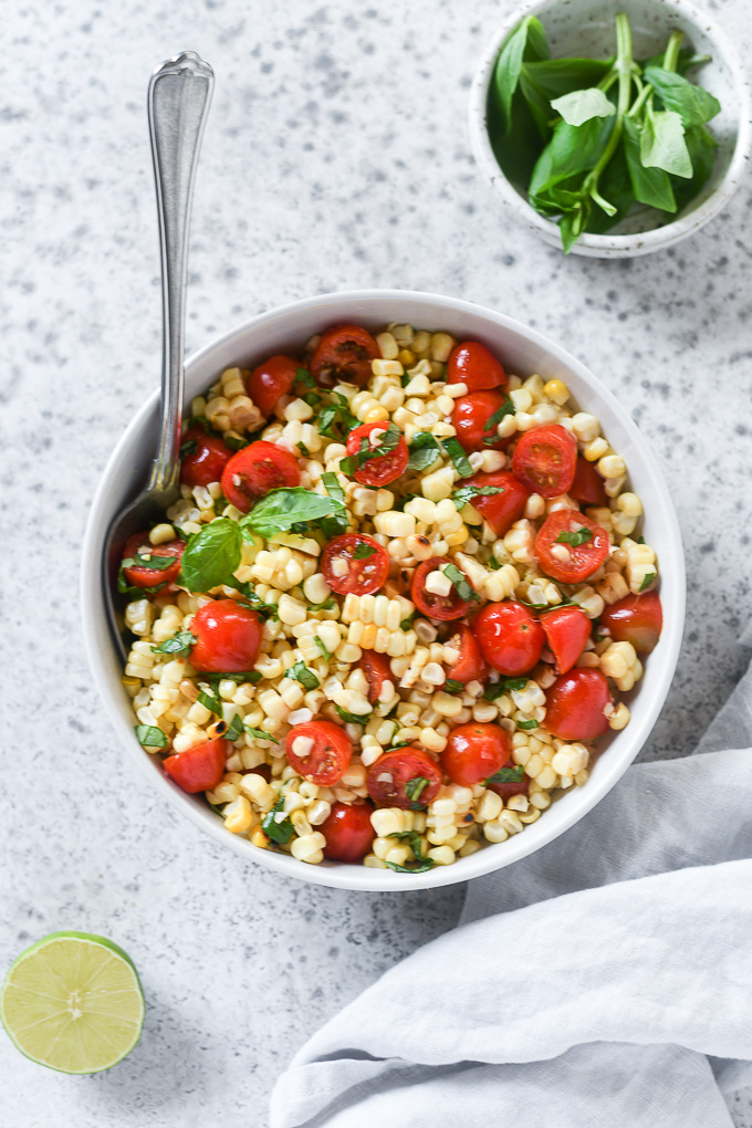 Tomato corn salad in a white bowl with basil