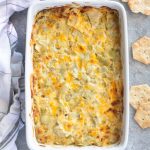 Hot artichoke dip in a baking dish with crackers