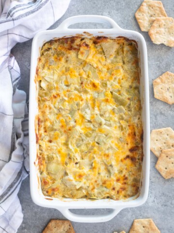 Hot artichoke dip in a baking dish with crackers