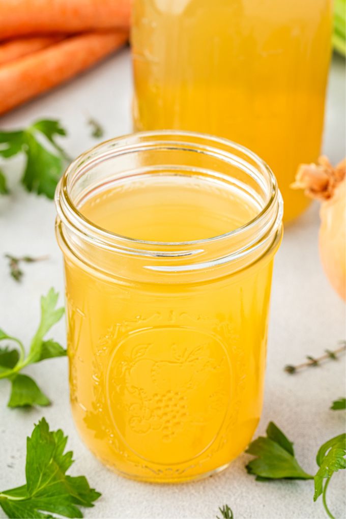 Homemade chicken stock in a jar with ingredients surrounding it
