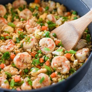 Wooden spoon digging into pan of shrimp fried rice