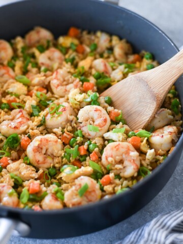 Wooden spoon digging into pan of shrimp fried rice