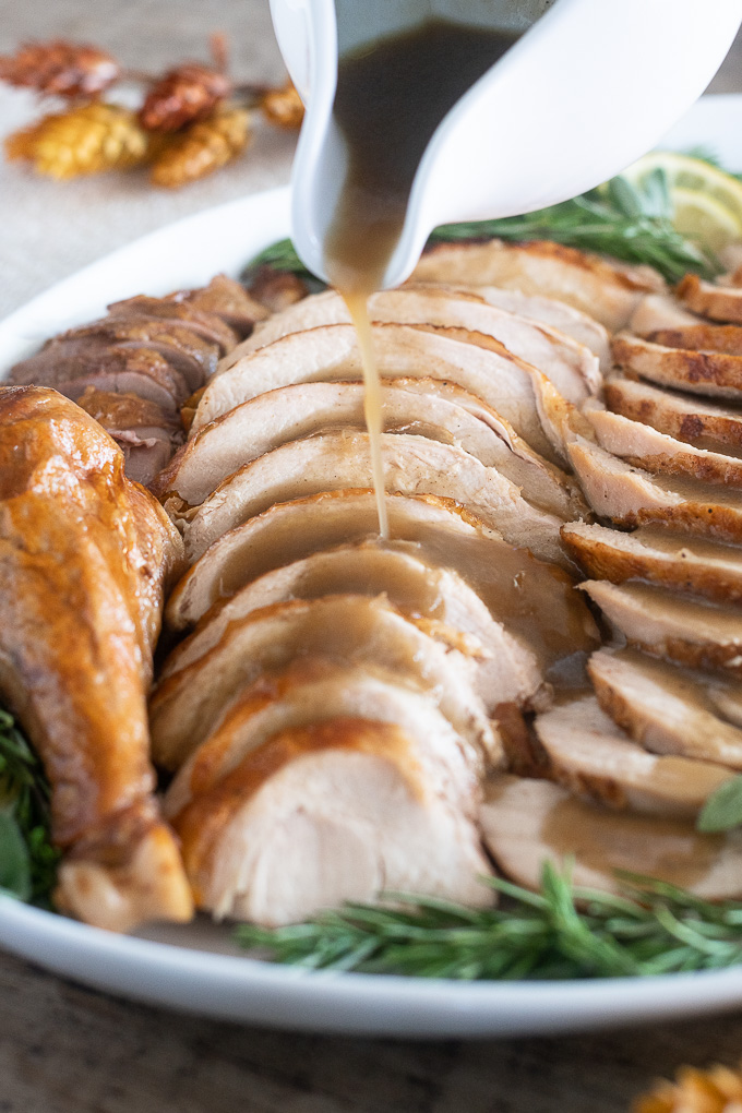 roast turkey sliced on a platter with gravy pouring