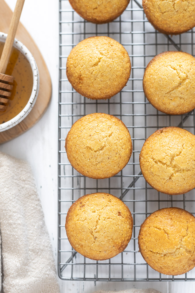 Corn muffins on a wire rack next to bowl of honey