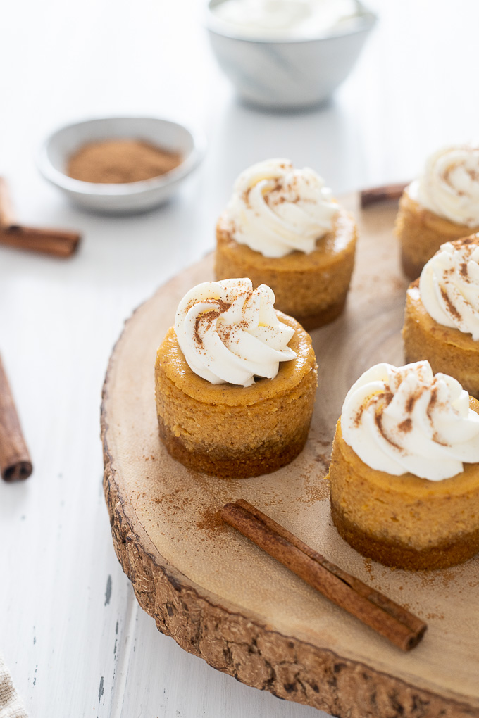 Mini pumpkin cheesecakes on a serving tray with cinnamon sticks