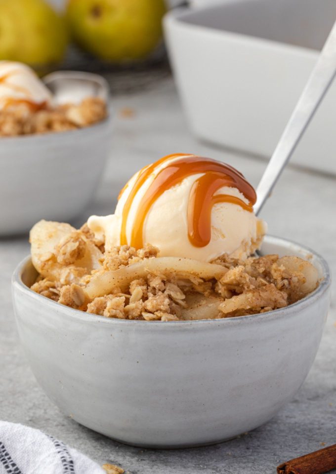 Pear crisp in a bowl with ice cream and caramel