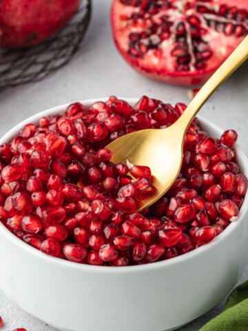 Spoon digging into bowl of pomegranate seeds