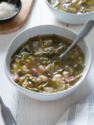 Bowl of escarole and bean soup with spoon buried inside