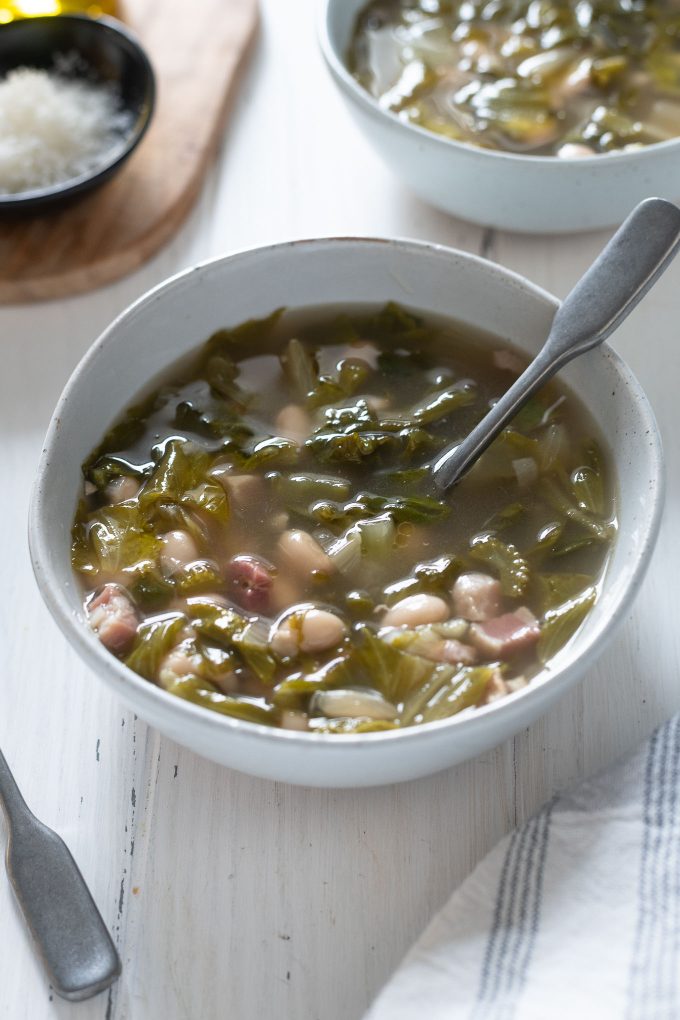 Bowl of escarole and bean soup with spoon buried inside