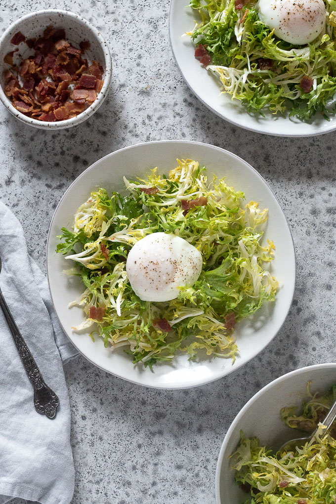 Plates of salad lyonnaise with bacon and frisee in bowls