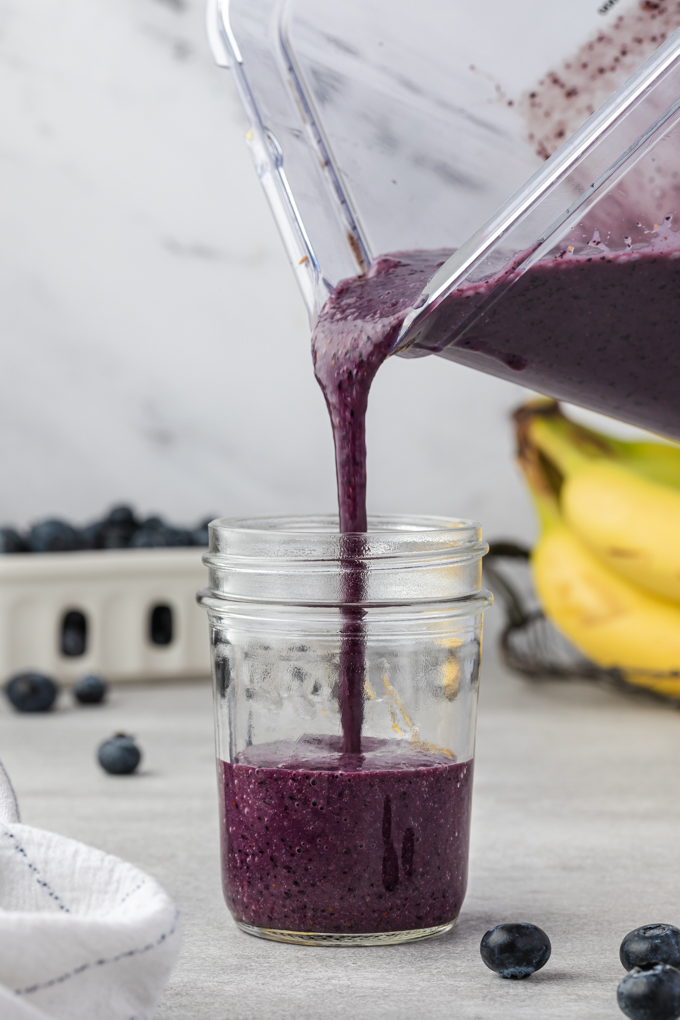 Pouring blueberry banana smoothie into a jar