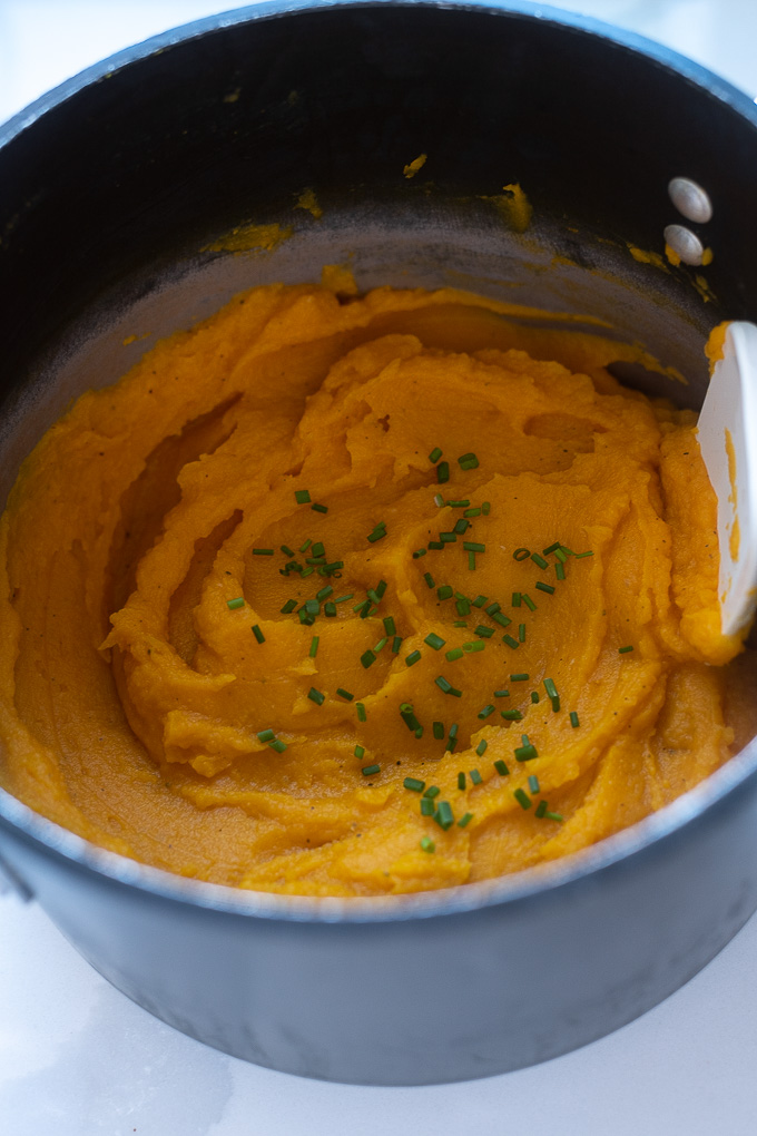 Mashed butternut squash in a pot with chives on top