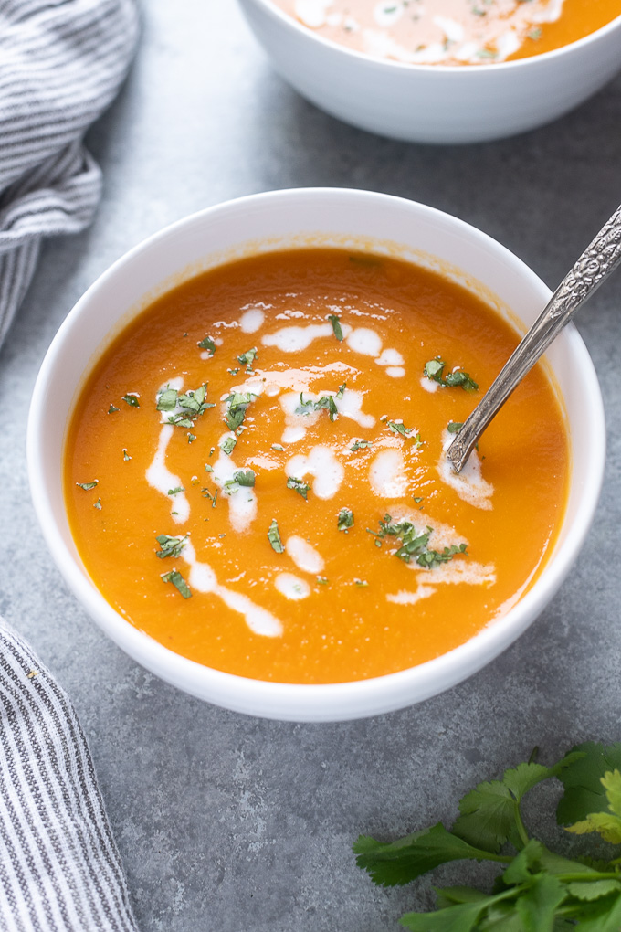 Carrot soup in a white bowl with spoon digging in