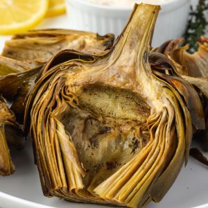 Roasted artichokes on a platter with aioli and lemon