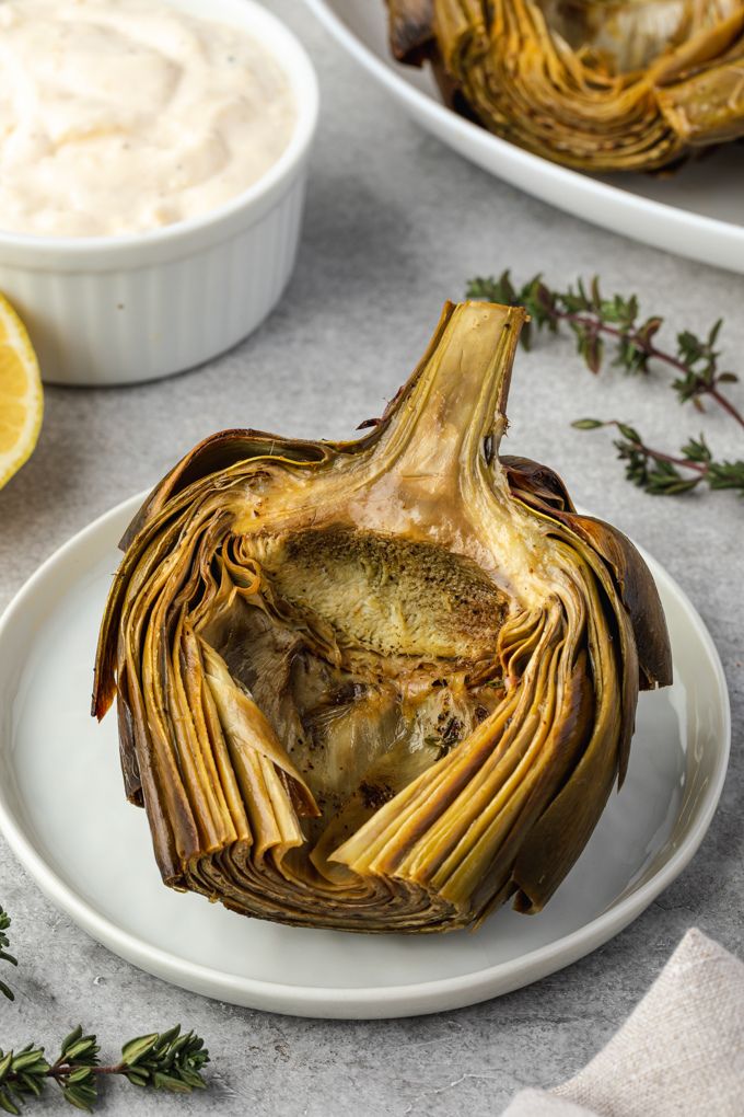 Roasted artichoke on a plate with aioli and thyme