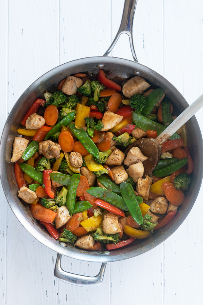 Chicken and vegetable stir fry in a skillet with wooden spoon