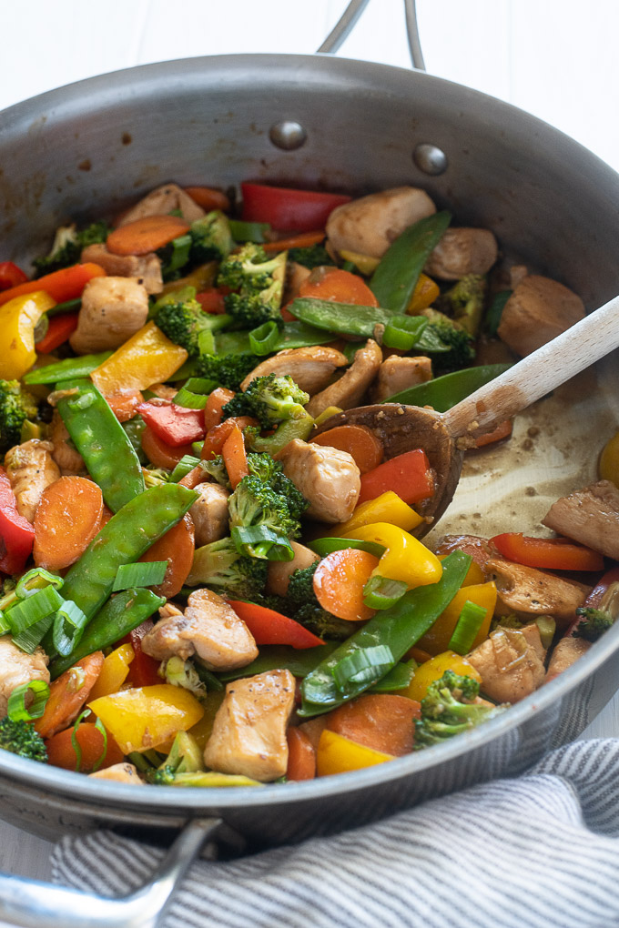 Chicken veggie stir fry in a skillet with wooden spoon digging in