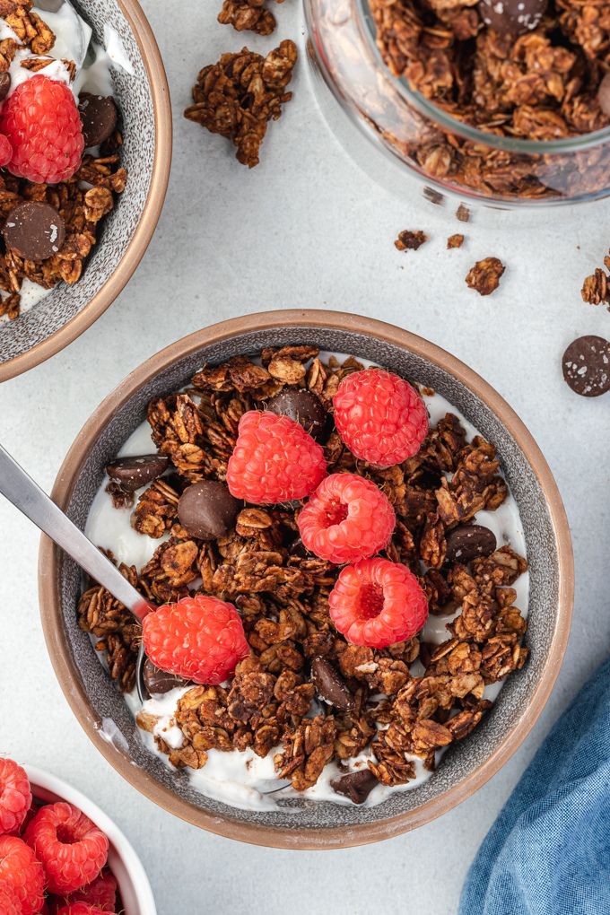 Chocolate granola in a bowl with milk, raspberries and a spoon