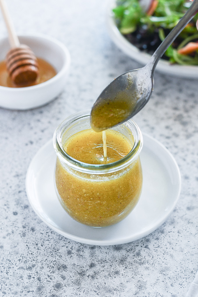 spoon drizzling honey mustard dressing into a jar