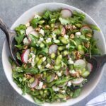 Asparagus salad in a white bowl with salad servers digging in